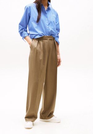 Chemise boutonnée rayée bleu et blanc, associée à un pantalon large marron et des baskets blanches. Le tissu semble lisse et léger.