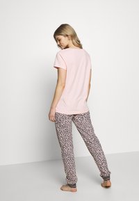 Roze katoenen t-shirt met korte mouwen, gecombineerd met een broek met luipaardprint en zwart-witte gestreepte manchetten. Soepele textuur, relaxte pasvorm.