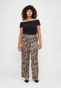 Μαύρη, εκτός ώμου μπλούζα με πλισέ σχέδιο; καφέ παντελόνια σε χαλαρή γραμμή με κυματιστό μαύρο και λευκό σχέδιο; μαύρα παπούτσια με λεπτομέρειες.