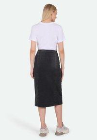 Sort denim midi-skirt med en tætsiddende form, synlige syninger og høj talje. Kombination med en simpel hvid T-shirt og sneakers.