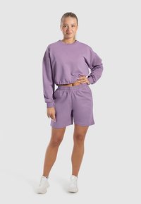 Lila sweatshirt van een katoenmix met elastische zoom, gecombineerd met bijpassende shorts met elastische tailleband. Model staat tegen een neutrale achtergrond.