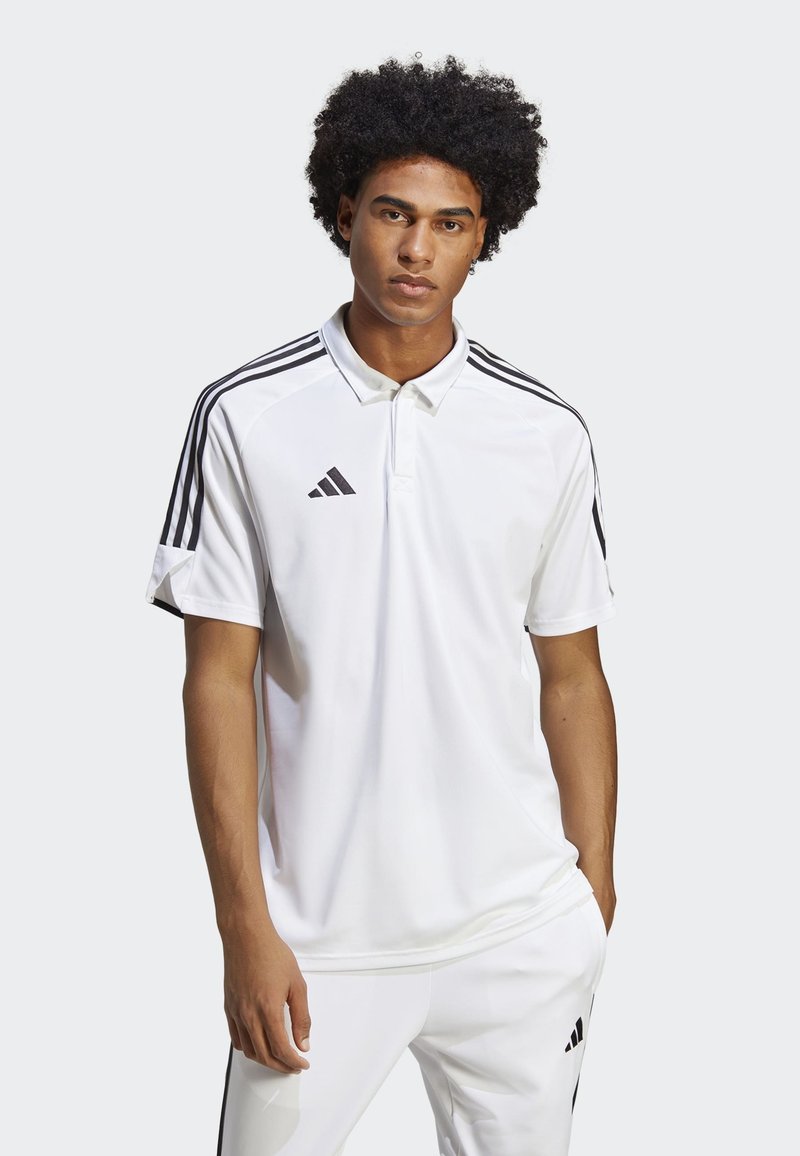 Maglietta polo bianca con design a tre strisce nere sulle spalle, dotata di colletto con bottoni e piccolo logo del brand nero sul petto.