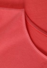 Tessuto di cotone corallo con una texture liscia, caratterizzato da un collo rotondo e cuciture piatte, che mostrano un bordo piegato.