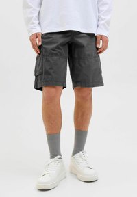 Pilki krovinių šortai su šoninėmis kišenėmis, pagaminti iš medvilninio twill audinio, kelių ilgio, derinami su pilkomis kojinėmis ir baltais sportbačiais. Atsitiktinis dizainas.