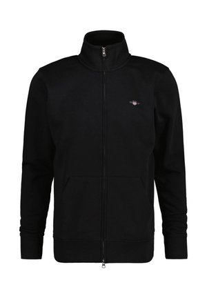 Sweat-shirt zippé noir avec col haut, comportant deux poches avant et des poignets côtelés. Le tissu semble lisse et doux. Petit logo sur la poitrine.