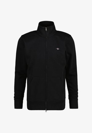 Sudadera negra con cremallera y cuello alto, con dos bolsillos frontales y puños acanalados. El material parece suave y liso. Logotipo pequeño en el pecho.