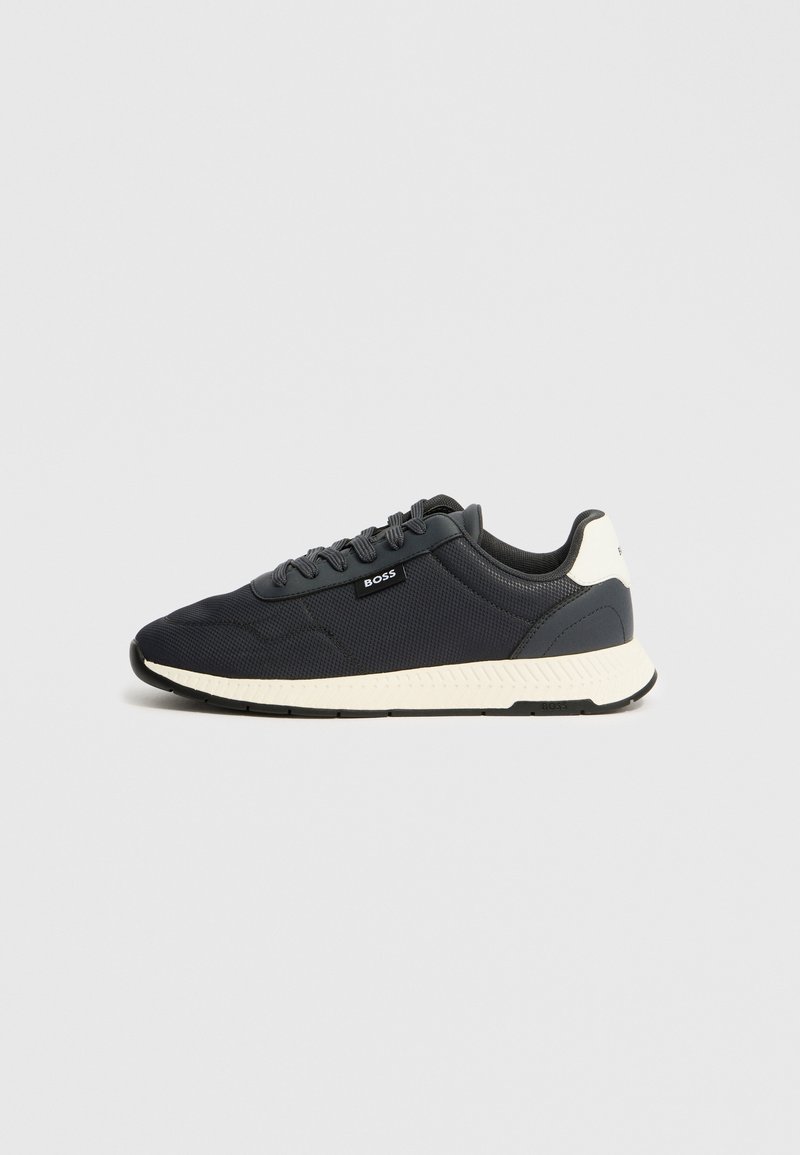 Baskets bleu foncé avec un dessus en tissu texturé, semelle blanche et accents ton sur ton ; elles comportent des lacets et un petit logo sur le côté.