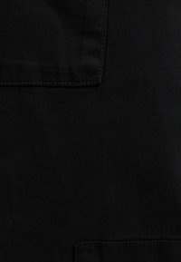 Svart tyg som visar en platt textur med synliga sömmar. Har en ficka med rena kanter. Materialet verkar hållbart och slätt.