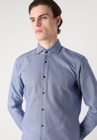 Camicia a quadri blu con maniche lunghe, leggero lucido e colletto strutturato. Presenta bottoni blu e una vestibilità aderente.