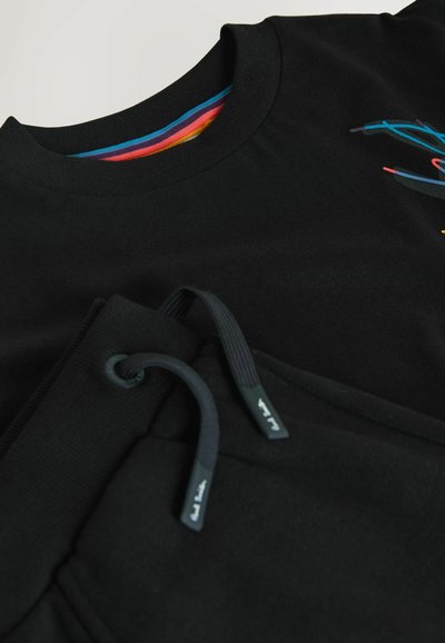 Ensemble sweat-shirt noir et pantalon de survêtement avec col intérieur à rayures colorées et cordons décorés de petits textes blancs aux extrémités.