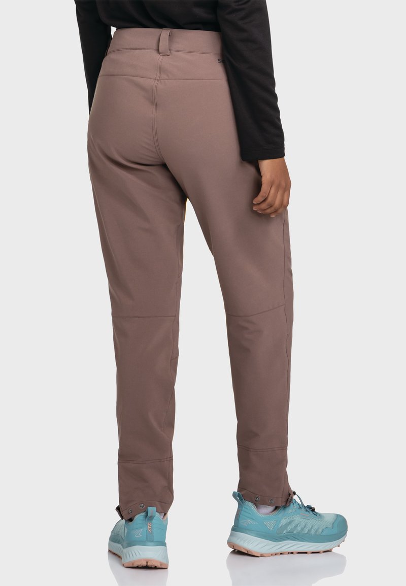 Braune Outdoorhosen mit Slim Fit, aus weichem Material gefertigt, mit flachen Nähten und kombiniert mit hellblauen Wanderschuhen.