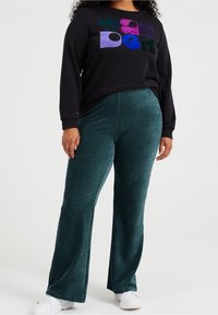 Czarna bluza z kolorowym napisem "wonder", sparowana z ciemnozielonymi, żebrowanymi spodniami z korduroy. Białe sneakersy dopełniają stylizację.