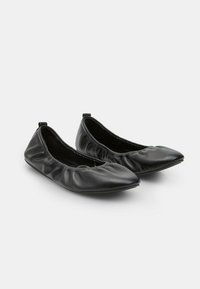 Zapatos planos negros de cuero suave, con punta redondeada, elástico fruncido en los laterales y suela de perfil bajo.