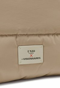 Beige padded bag featuring a fabric texture, with a white label displaying "UNIO HAMBURG X LES VISIONNAIRES" in black and red print.