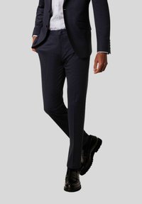 Donkerblauwe op maat gemaakte broek van gestructureerde stof, met een slim fit, zijzakken en een gladde afwerking, gecombineerd met zwarte schoenen.