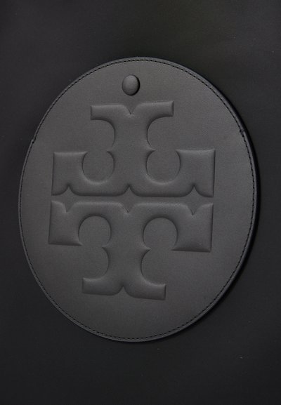 Pachet rotund din piele neagră, cu un design geometric embossat și un punct în partea de sus, atașat de o suprafață texturată neagră.
