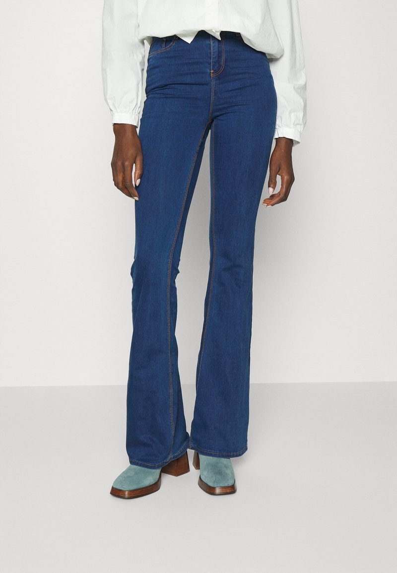 Uppblåsta blå jeans i denim, med hög midja, kontrasterande sömmar och en mjuk yta, i kombination med teal-höljarstövlar.