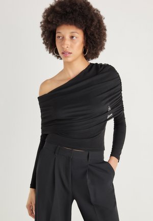 Top nero con una spalla realizzato in tessuto morbido con texture arricciata; design aderente abbinato a pantaloni neri a vita alta.