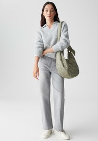 Lichtgrijze fuzzy trui met een kraag, gecombineerd met lichtgekleurde rechte jeans en witte sneakers. Houdt een doorgestikt olijfgroene schoudertas vast.