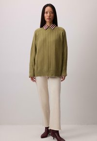 Olive rohelise ribaga soe särk punase ja valge triibulise kaelusega, kombineerituna kreemjavärvi laienevate pükste ja burgundia värvi sõrmedega saapatega.