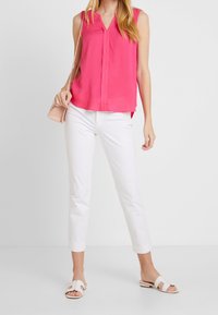 Haut sans manches fuchsia avec un décolleté en V et une patte de boutonnage, associé à un pantalon droit blanc et des sandales blanches à enfiler.