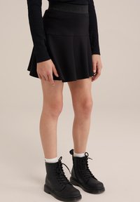 Falda negra acampanada hecha de una tela suave con una cintura ajustada. Combinada con botas negras de cordones y calcetines blancos hasta el tobillo.