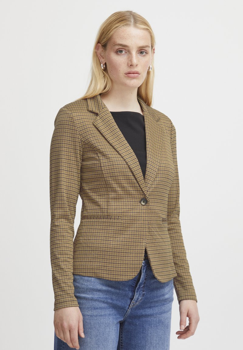 Brun rutig blazer med en figurnära design, enkel knappstängning och två framfickor, parat med en svart topp och blå jeans.