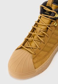 Ταμ suede αθλητικά παπούτσια με υφασμάτινη καπα και χρυσές λεπτομέρειες. Ο σχεδιασμός περιλαμβάνει τρεις πλευρικές ρίγες για επιπλέον λεπτομέρεια.