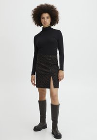 Un top negru cu guler înalt asociat cu o fustă cu model zebră maro, care are o fante pe față și detalii cu nasturi, completată de cizme maro până la genunchi.