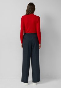 Czerona bluzka z długim rękawem połączona z ciemnoszarymi spodniami o wysokim stanie i szerokich nogawkach. Dzianinowa faktura bluzki, gładki materiał spodni z subtelnymi paskami.