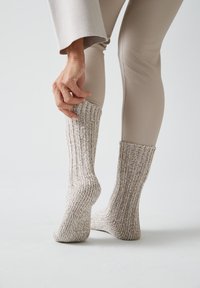 Calcetines de punto con una textura acanalada, principalmente beige con acentos moteados. Los lleva una persona que se los sube mientras está sentada.