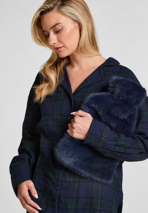 Marine geruite overhemd met lange mouwen in groen en wit, gecombineerd met een donzige donkerblauwe bontaccessoire, tegen de borst gehouden.