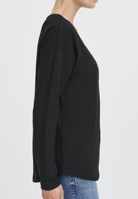 Schwarzes Langarmshirt mit V-Ausschnitt, aus weichem Stoff gefertigt. Verfügt über eine lockere Passform und schlichte Gestaltung, kombiniert mit blauen Jeans.