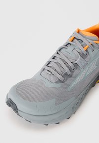Grå trail løbesko med en åndbar mesh-overdel, orange accenter og en tekstureret gummisål med slidbane.