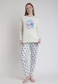 Camisa de pijama de manga larga en crema con estampado de animales de dibujos animados; combinada con pantalones blancos que presentan un patrón colorido de animales y finas rayas verticales.