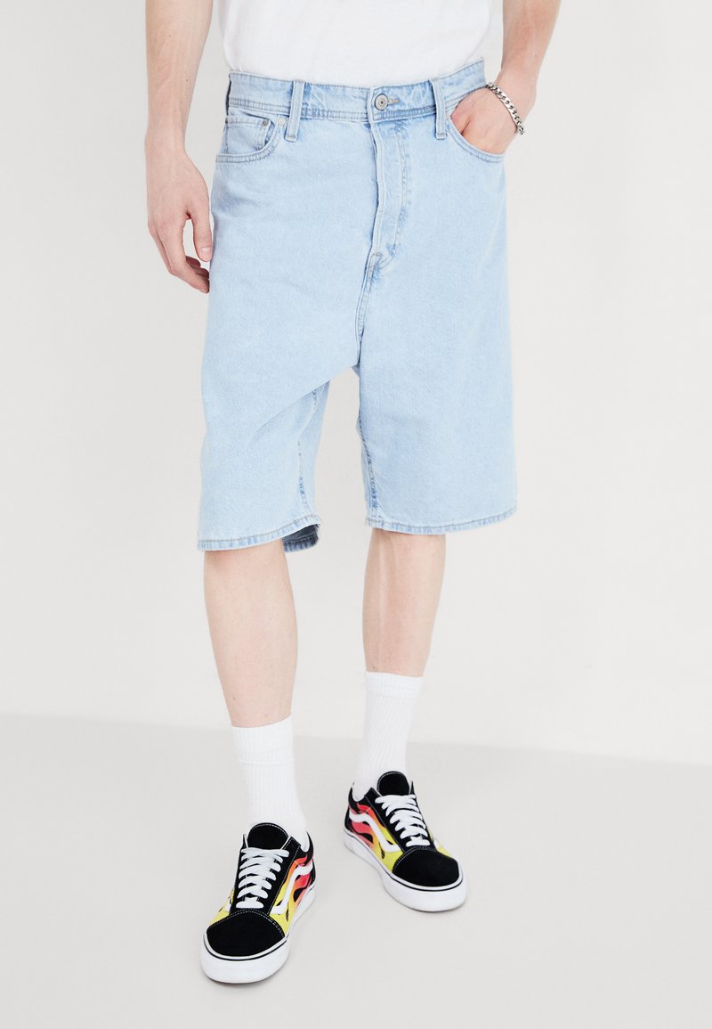 Lyseblå denimshorts med en avslappet passform, med et klassisk fem-lomme-design og rå kant. Kombinert med svarte sneakers og hvite sokker.