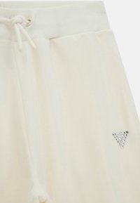 Pantaloni della tuta color crema con una texture morbida, dotati di vita elastica, cordoncino e un accento di strass triangolare sul lato.