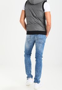 Grå vadderad väst med huva, svart nederdel, bärs över en vit t-shirt. Slim-fit ljusblå jeans och vita sneakers kompletterar outfiten.