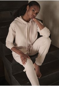 Set di abbigliamento loungewear a coste beige realizzato in tessuto morbido, composto da una maglia con cappuccio e cordoncino e pantaloni coordinati con vita elastica.