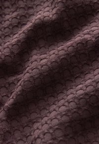 Teksturowana tkanina w ciemnym brązie z wzorem plastra miodu. Materiał ma miękką, lekko wypukłą powierzchnię i ogólnie gładką fakturę.