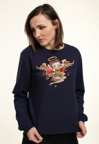 Felpa blu navy con scollo rotondo e maniche lunghe, caratterizzata da una grafica di un personaggio alato con un banner che recita "Lil' Angel."