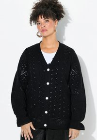 Černý pletený cardigan s V-výstřihem, přesměrovanými rukávy a dekorativními výřezy. Dokončeno velkými bílými knoflíky.