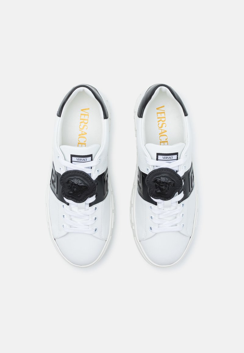 Weiße Ledersneaker mit einem schwarzen Mittelband, das ein markantes schwarzes Löwenkopf-Detail und eine weiße Schnürung aufweist. Goldenes "VERSACE"-Logo im Inneren.