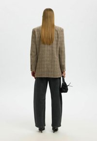 Blazer surdimensionné à carreaux bruns avec des épaules structurées, associé à un jean foncé taille haute et un petit sac à main noir, au design minimaliste.