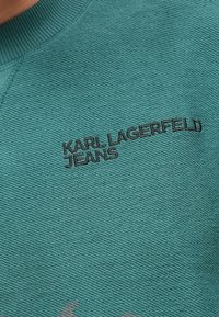 Tyrkysová mikina s texturovanou tkaninou, žebrovaným výstřihem a vyšívaným logem "KARL LAGERFELD JEANS" v černé barvě.