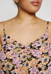 Blommig spets som har en svart bakgrund med rosa, gula och blå blommor. Tjocka remmar och en subtil rynkad detalj vid halsringningen.