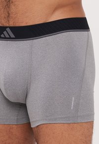 Szürke sportos boxer alsónemű fekete bordás derékpánttal, logóval, rugalmas, nedvességelvezető tulajdonságú anyagból készült.
