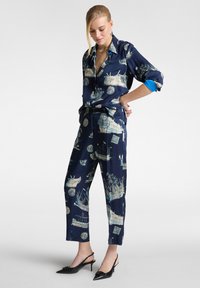 Completo di camicia e pantaloni in raso blu navy, con stampa marittima in crema, polsini arrotolati e design slim-fit, abbinato a tacchi a punta neri.