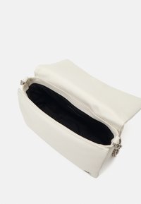 Krémová kožená kabelka přes rameno s otevřeným klapkem, černou vnitřní podšívkou a detaily stříbrného řetězového popruhu.