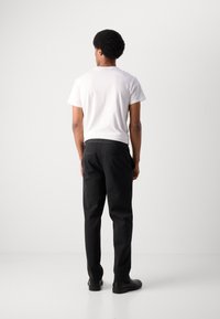 Pantalon noir à coupe décontractée, avec des poches arrière et une taille élastique, associé à un t-shirt blanc ajusté.